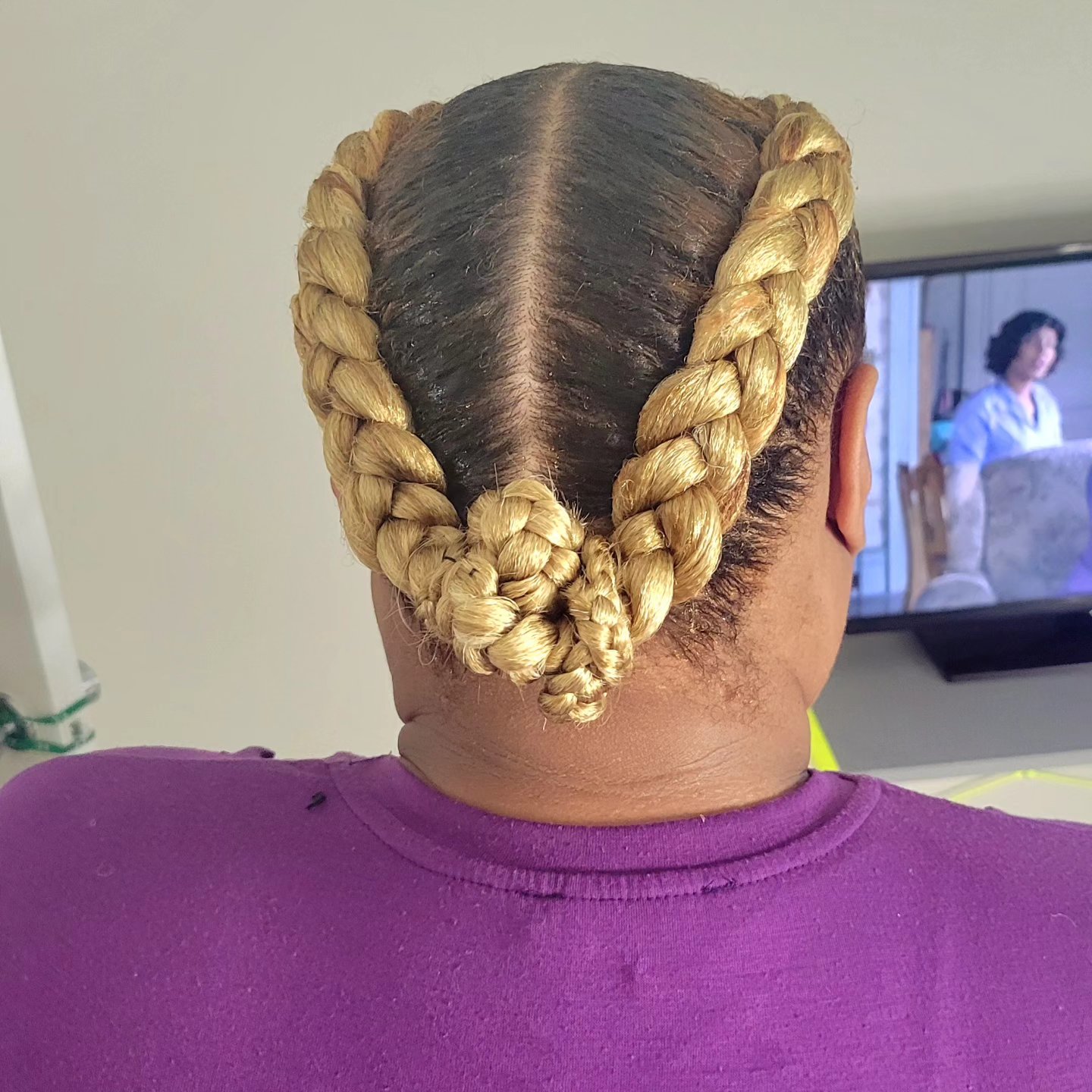 Blonde feed-in braids gathered into two low buns at the nape, back view