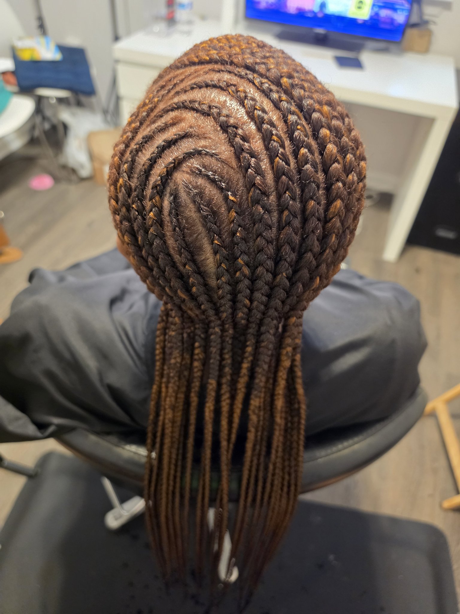 Curved feed-in cornrows in auburn brown seen from behind