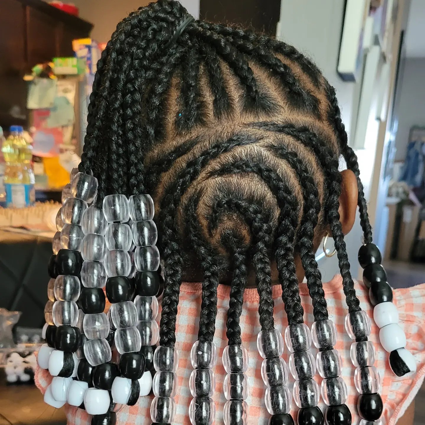 Kids braids with clear, black and white beads on a young girl, back view showing swirl cornrow pattern